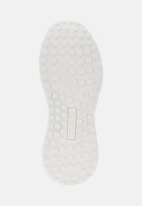 Semelle de chaussure en caoutchouc blanc avec un motif de renfoncements circulaires et un logo rectangulaire central embouti avec "GUESS."