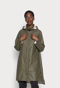 Cappotto impermeabile verde oliva con cappuccio, dotato di tasche frontali, fodera interna chiara a contrasto e bottoni a pressione lungo l'orlo.