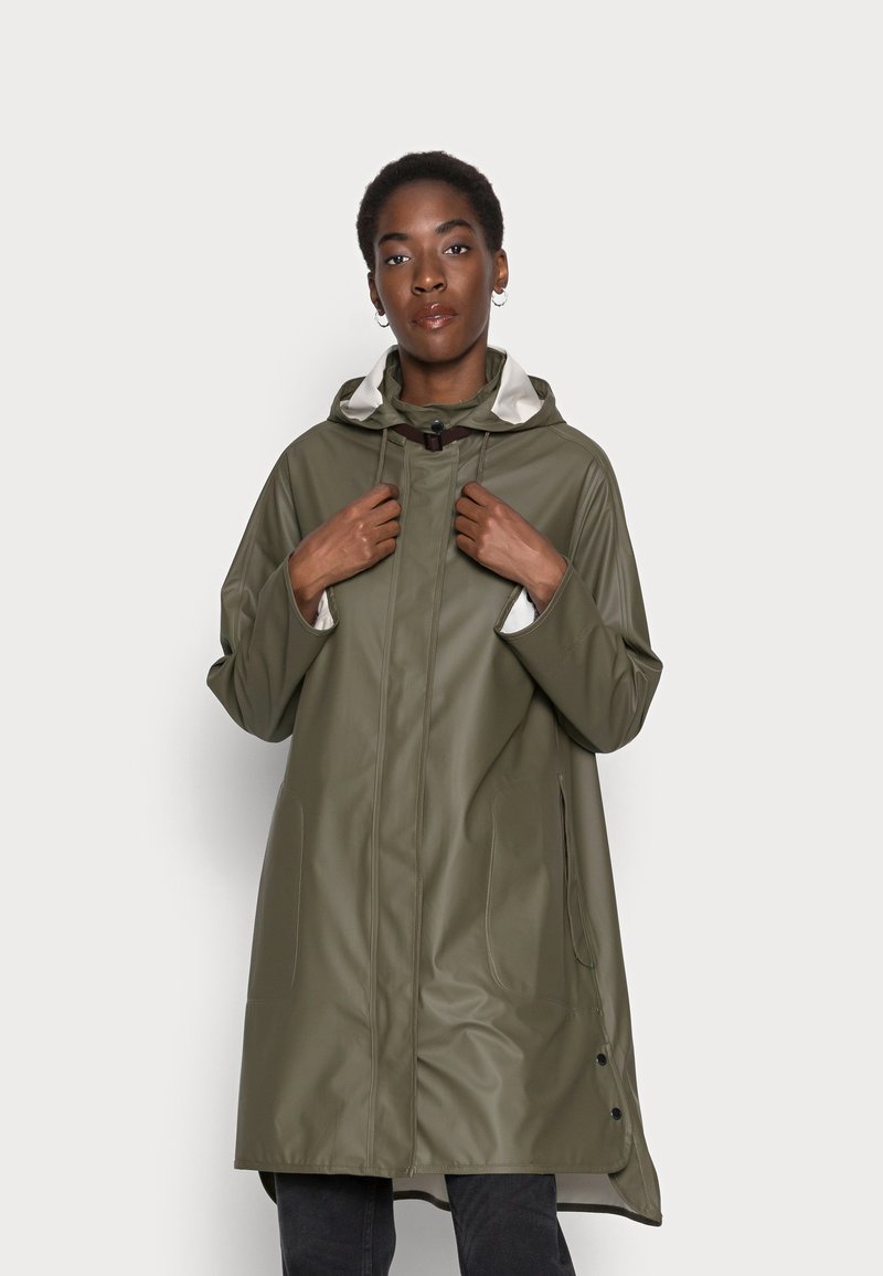 Cappotto impermeabile verde oliva con cappuccio, dotato di tasche frontali, fodera interna chiara a contrasto e bottoni a pressione lungo l'orlo.