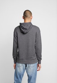 Grå huvtröja med mjuk textur, försedd med dragsko och ribbade muddarna. Bärs tillsammans med ljusblå denimjeans.