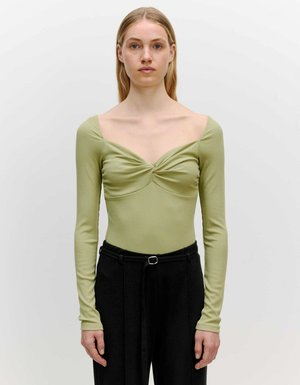 Langsleeve, ribbeltop in lichtgroen met een hartvormige halslijn en geplooide details bij de buste, gecombineerd met zwarte high-waisted broeken.