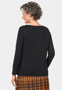 Schwarzes Langarmshirt aus weichem Stoff mit weitem Rundhalsausschnitt und lockerer Passform. Sichtbares strukturiertes Muster auf einem orangefarbenen Karo-Rock.