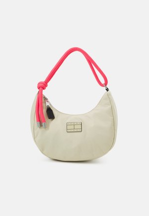 Beige olan hilal şeklinde omuz çantası, parlak pembe ip kulp ve ön kısmında "Tommy Jeans" yazılı metal logo plakası bulunmaktadır.