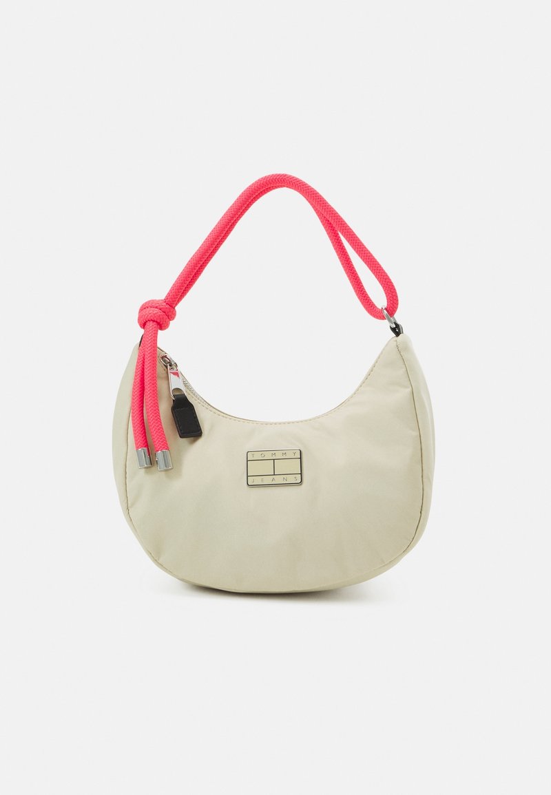 Beige halvmåneformad axelväska med ett lysande rosa rephandtag och en frontplåt i metall med texten "Tommy Jeans."