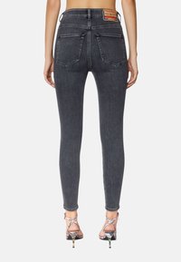 Jeans ajustados en denim gris oscuro, con una cintura alta, dos bolsillos traseros y una etiqueta de cuero con la marca en la cinturilla. Los zapatos son con tiras.