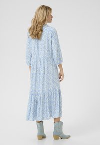 Gaiši zila ziedu kleita ar trim ceturtdaļām piedurknēm, ar slāņotiem volāniem apakšmalā, apvienota ar gaiši zilām cowboy zābakiem. Mīksta kokvilnas auduma.