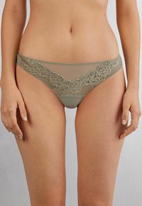Olijfgroen kant en doorzichtige mesh bikini ondergoed met bloemmotieven langs de tailleband en zijkanten. Soepele stof met een delicate afwerking.