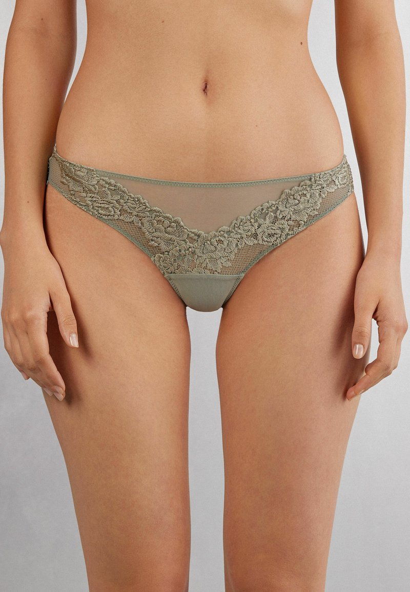 Olijfgroen kant en doorzichtige mesh bikini ondergoed met bloemmotieven langs de tailleband en zijkanten. Soepele stof met een delicate afwerking.
