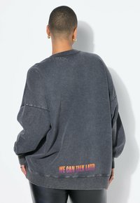 Sudadera gris de gran tamaño con cuello redondo, que presenta el texto "PODEMOS HABLAR MÁS TARDE" en colores degradados en la parte trasera cerca del dobladillo.