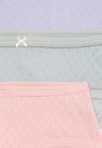 Tre paia di mutandine in cotone piegate: lavanda, grigia con dettaglio a fiocco e rosa, ciascuna con piccoli motivi a occhio e rifiniture in pizzo.