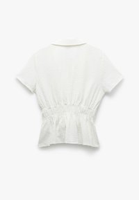 Hvid peplum top med korte ærmer, der har et tekstureret stof og elastisk talje for en tætsiddende silhuet. Klassisk krave design.