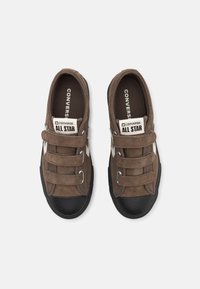 Zapatillas de ante marrón con dos correas de Velcro, puntera de goma negra y logo de Converse blanco en la lengüeta y el lateral.