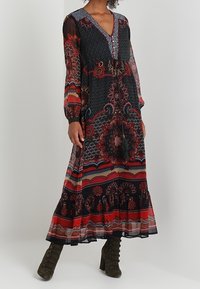 Maxiklänning med djup V-ringning, långa genomskinliga ärmar, mångfärgade blommönster och geometriska mönster, volangkant och markerad midja.