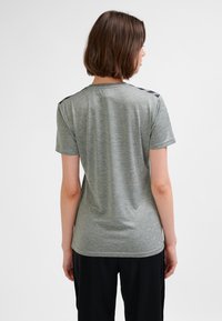 Grå t-shirt med korta ärmar, tillverkad av mjukt tyg, med en slät yta och svarta accenter på axlarna. Enkel och tajt passform.