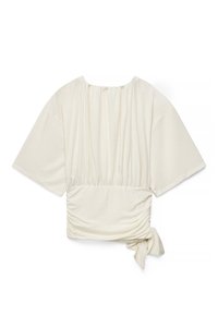 Blusa color crema con mangas anchas, escote elástico fruncido, cintura fruncida y detalle de lazo lateral sobre fondo blanco.
