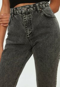 Jeans de tiro alto en denim negro con una textura ligeramente desgastada, que cuentan con cierre de botón, bolsillos frontales y costuras en contraste.