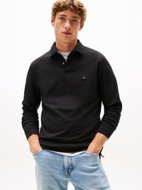 Juodas ilgomis rankovėmis polo mar�škinėliai su apykakle, turintys mažą logotipą kairėje krūtinės pusėje, derinami su šviesiai mėlynomis džinsinėmis kelnėmis.