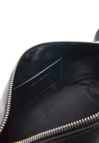 Interno di una borsa in pelle nera con una trama liscia, chiusura con zip e una piccola fessura per schede o documenti contro un rivestimento scuro.