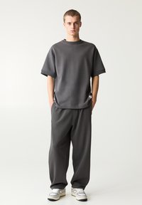 Grijze oversized t-shirt met korte mouwen, gecombineerd met bijpassende grijze losse broek. Gecombineerd met witte sneakers met zwarte accenten.