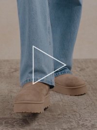 Světle hnědé semišové nazouvací boty s tlustou, texturovanou podrážkou, spárované s světle modrými džínami. Boty mají hladký, zaoblený design.