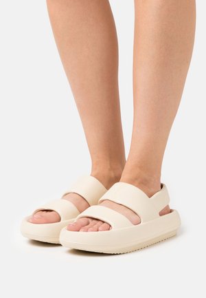 Sandales couleur crème avec deux larges brides sur le pied, design ouvert à l'avant, semelle épaisse et finition texturée pour plus d'adhérence.