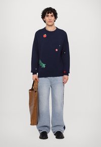 Marineblauer Pullover mit bunten bestickten Akzenten, lockere Passform, gerippte Bündchen und Saum. Kombiniert mit hellblauen, weiten Jeans und einer braunen Tasche.