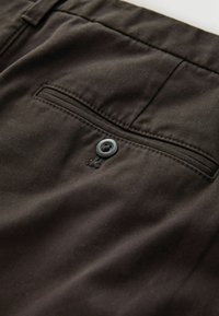 Dark brown trousers made of smooth cotton fabric, featuring a back pocket with a gray button and subtle stitching detail.