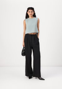 Světle modrý bezrukávový top zkombinovaný s černými širokými kalhotami. Modelka drží malou černou tašku; outfit se vyznačuje čistými liniemi a uvolněným střihem.