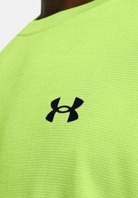 Neon-grünes Sportshirt aus strukturiertem Stoff mit einem schwarzen Under Armour-Logo auf der Brust. Rundhalsausschnitt.