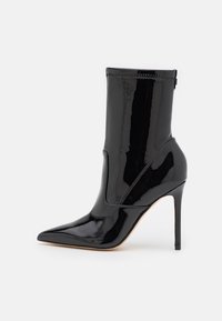 Czarne lakierowane botki za kostkę z szpiczastym noskiem i wysokim obcasem w szpic. Posiadają bezszwową cholewkę z elastycznymi panelami po bokach dla łatwości zakładania.