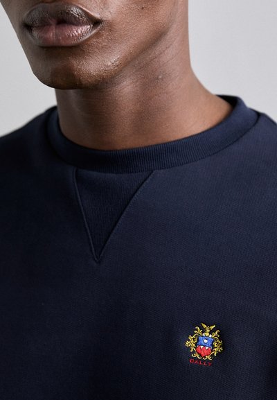 Navy blue sweatshirt made of textured cotton, featuring a crew neck and a small, embroidered multicolored logo on the chest.