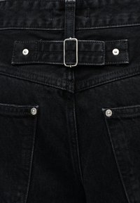 Οπίσθια όψη μαύρων τζιν από denim με δύο τετράγωνα τσέπες με ασημί εμπριμέ και οριζόντια ρυθμιζόμενη λωρίδα με μεταλλική αγκράφα.