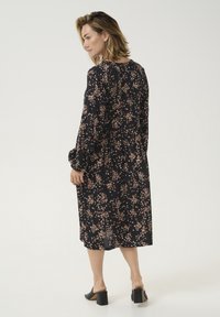 Black floral dress with long sleeves, cinched waist, and knee-length hem. Features small pink and white floral patterns. Pair of black block heel shoes.
