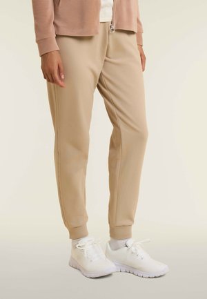 Pantalons de jogging beiges avec une taille élastique et des chevilles fuselées, associés à des chaussures de sport blanches avec un design en maille texturée.