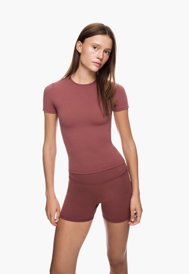 Mauve sporttop met korte mouwen, gecombineerd met bijpassende strakke shorts. Gladde textuur, eenvoudig ontwerp en getailleerde pasvorm.