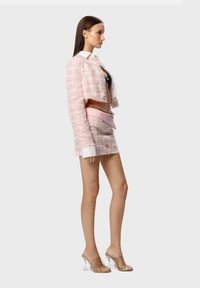 Giacca cropped in tweed rosa, gonna mini abbinata con bottoni e sandali con tacco trasparente. Presenta una camicia colletto sotto la giacca.
