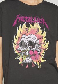 Černé bavlněné tričko s barevným grafickým potiskem lebky s květinami a kostmi, zvýrazněné živým žlutým a růžovým pozadím.
