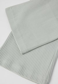 Vaaleanvihreä röyhelötila, jossa on pehmeä tekstuuri, puhtaat reunat ja hienot tikkausviivat. Kaksi taitettua palasta esitettyinä kerroksittain.