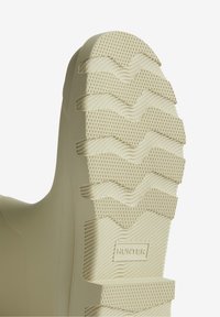 Semelle de botte en caoutchouc beige clair avec un motif texturé ondulé et des éléments d'adhérence triangulaires. Logo "HUNTER" embossé sur le côté.