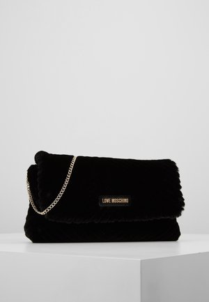 Black plush Love Moschino clutch bag with gold chain strap and logo plaque, displayed on white pedestal against gray background.