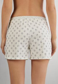 Witte katoenen shorts met bloemenpatroon en een elastische tailleband. De stof heeft kleine, donkere bloemenprints die gelijkmatig verspreid zijn.