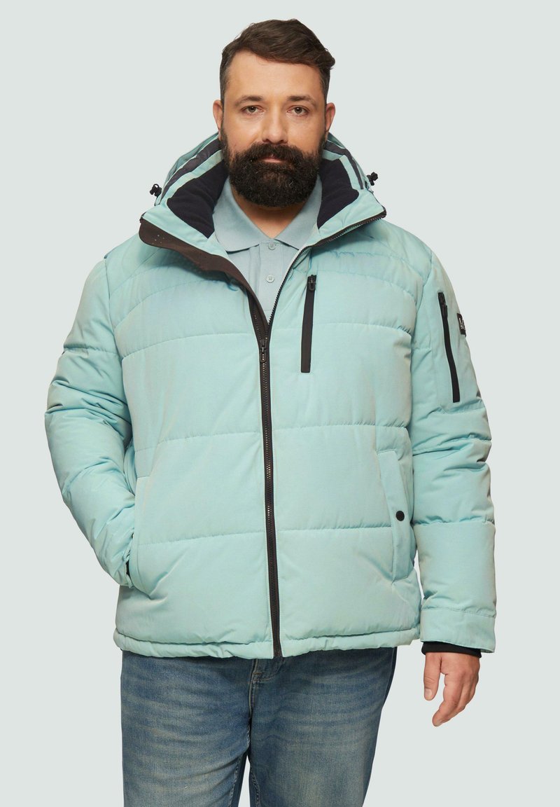 Jasnoniebieska kurtka puchowa z wysokim kołnierzem, zapięciem na zamek i czarnymi akcentami. Posiada pikowane sekcje oraz boczne kieszenie. Nosi się ją na szarym polo.