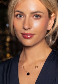 Gold-tone necklace featuring a central black circular pendant and two floral accents, with a thin chain and polished finish.