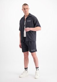 Korte mouwen, knoopsluiting shirt en bijpassende shorts in donkergrijs met een geometrische textuur. Heeft witte geborduurde branding. Witte sneakers.