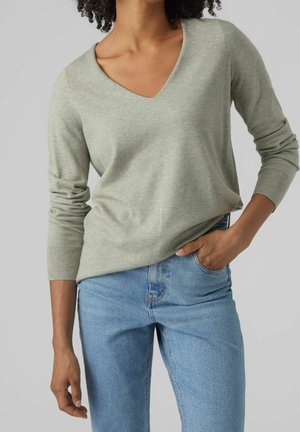 Maglione verde chiaro a V con polsini a coste, realizzato in materiale morbido, abbinato a jeans azzurri, che sottolineano una vestibilità rilassata.