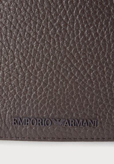 Surface en cuir marron texturé avec le logo Emporio Armani embossé près du bord inférieur.