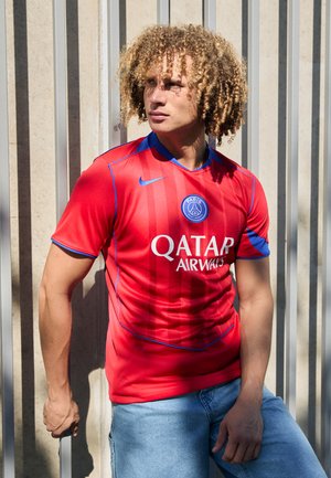 Jersey atlético rojo con acentos azules, con cuello redondo y rayas verticales llamativas. Muestra "QATAR AIRWAYS" en blanco, con un logo circular.