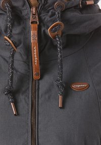 Tmavě šedá bunda s předním zipem, hnědými koženými detaily, kapucí se stahovací šňůrkou z opletených provázků a viditelnou nášivkou s logem.