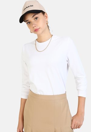 Witte lange mouwen shirt met een ronde hals, gecombineerd met beige high-waisted broek en een beige-zwart pet met de tekst "Book Club".