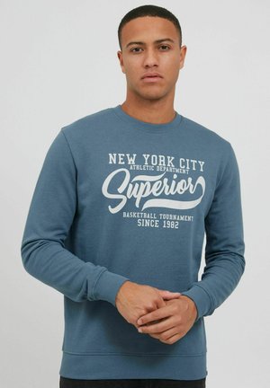 Plava dukserica od pamučne mješavine, s okruglim izrezom. Veliki bijeli natpis s natpisom "New York City Athletic Department Superior" i godinom.